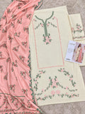 A flat-lay view of a traditional South Asian salwar suit set, featuring a cream-colored kurta with green and pink floral embroidery, a matching pink dupatta with green and pink floral patterns, and a folded matching fabric piece. A brand card for 'Zainab' is visible on the right side.