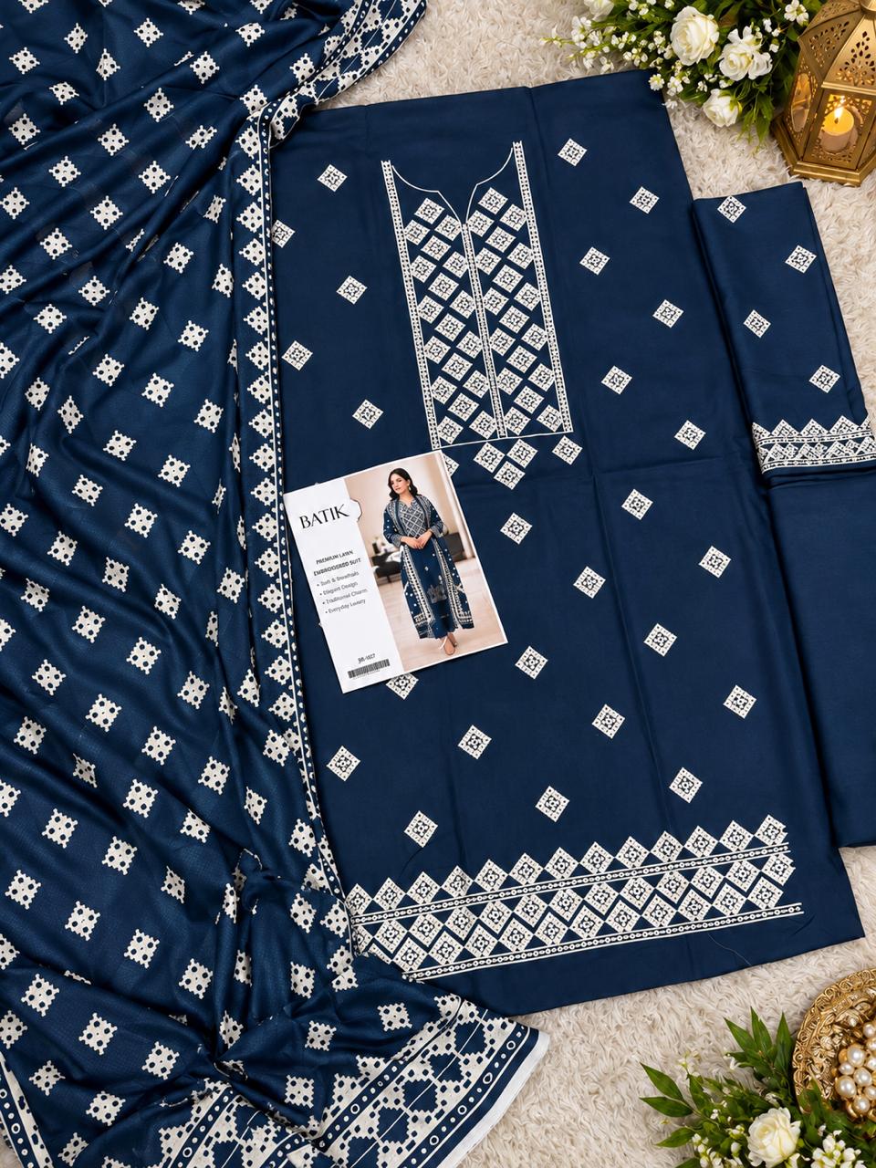 A navy blue salwar kameez suit set with intricate white embroidery, featuring a printed fabric card, draped dupatta, and matching trousers on a neutral textured background.