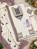 Cream-colored traditional Pakistani women's salwar suit set with intricate multicolor geometric embroidery, featuring a kurta, matching trousers, and a dupatta, styled on a soft white textured background with decorative floral and metallic props.