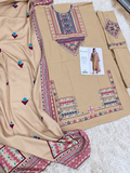 A beige three-piece salwar kameez suit set with colorful geometric embroidery on the neckline and borders, laid out on a white textured rug. The set includes a kameez tunic, matching trousers, and a dupatta with small embroidered motifs.