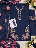 A navy blue women's shalwar suit set laid flat on a cream textured surface, featuring pink and gold floral embroidery around the neckline, hem, and dupatta border. A folded matching kurta piece, a dupatta, and a small printed card are arranged with the main fabric.