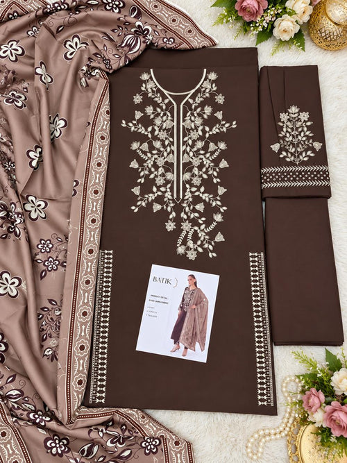 A flat-lay presentation of a brown three-piece salwar kameez suit set, featuring a kurta with intricate white floral embroidery, matching trousers, and a dupatta with matching floral patterns. A small brand card is visible on the kurta.